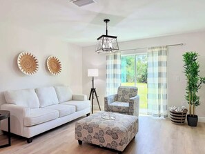 Ein Wohnzimmer mit einer Couch, Sesseln, einem Hocker, einer Stehlampe und einer Topfpflanze.