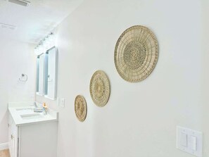 Ein Badezimmer mit einem weißen Waschbecken, einem Spiegel und drei gewebten Wanddekorationen.
