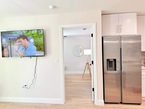 Eine moderne Küche mit einem Edelstahl-Kühlschrank, einem an der Wand montierten Fernseher und Holzboden.