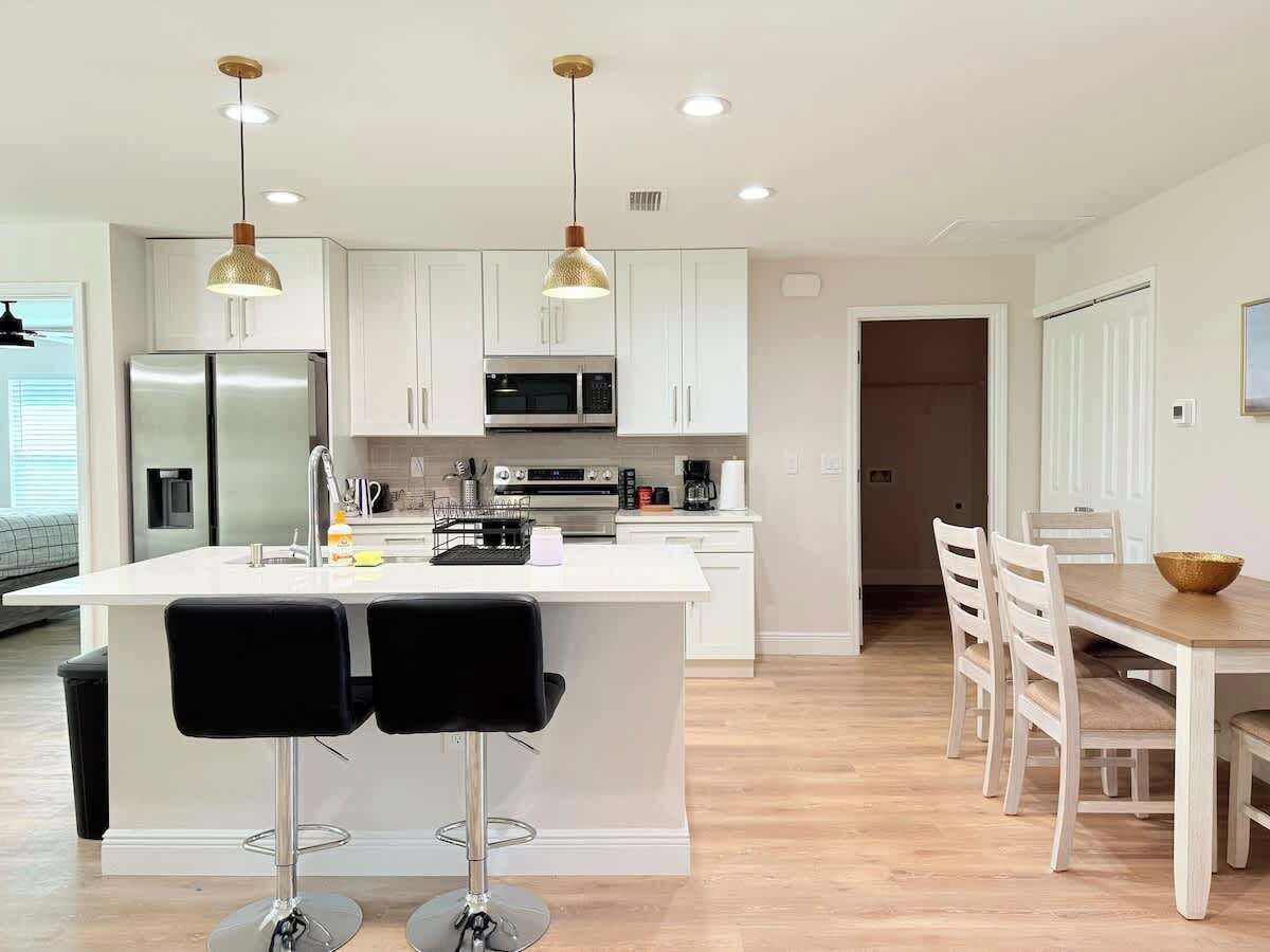 Una cocina moderna con armarios blancos, electrodomésticos de acero inoxidable y una isla central con taburetes de bar.
