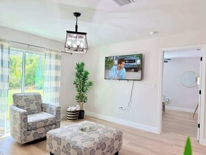 A living room with a sofa, a coffee table, a potted plant, a television, and a view of the outdoors through a glass door.