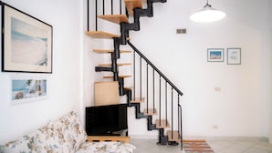 A modern living room with a staircase, a sofa, a television, and artwork on the walls.