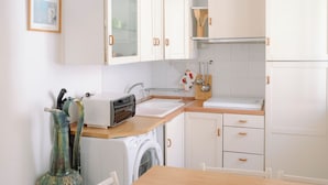 A kitchen with white cabinets, a wooden table, a ceiling fan, and a washing machine.