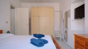A bedroom with a bed, two blue towels, a wooden wardrobe, a chair, and a wooden dresser.