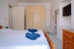 A bedroom with a bed, two blue towels, a wooden wardrobe, a chair, and a wooden dresser.