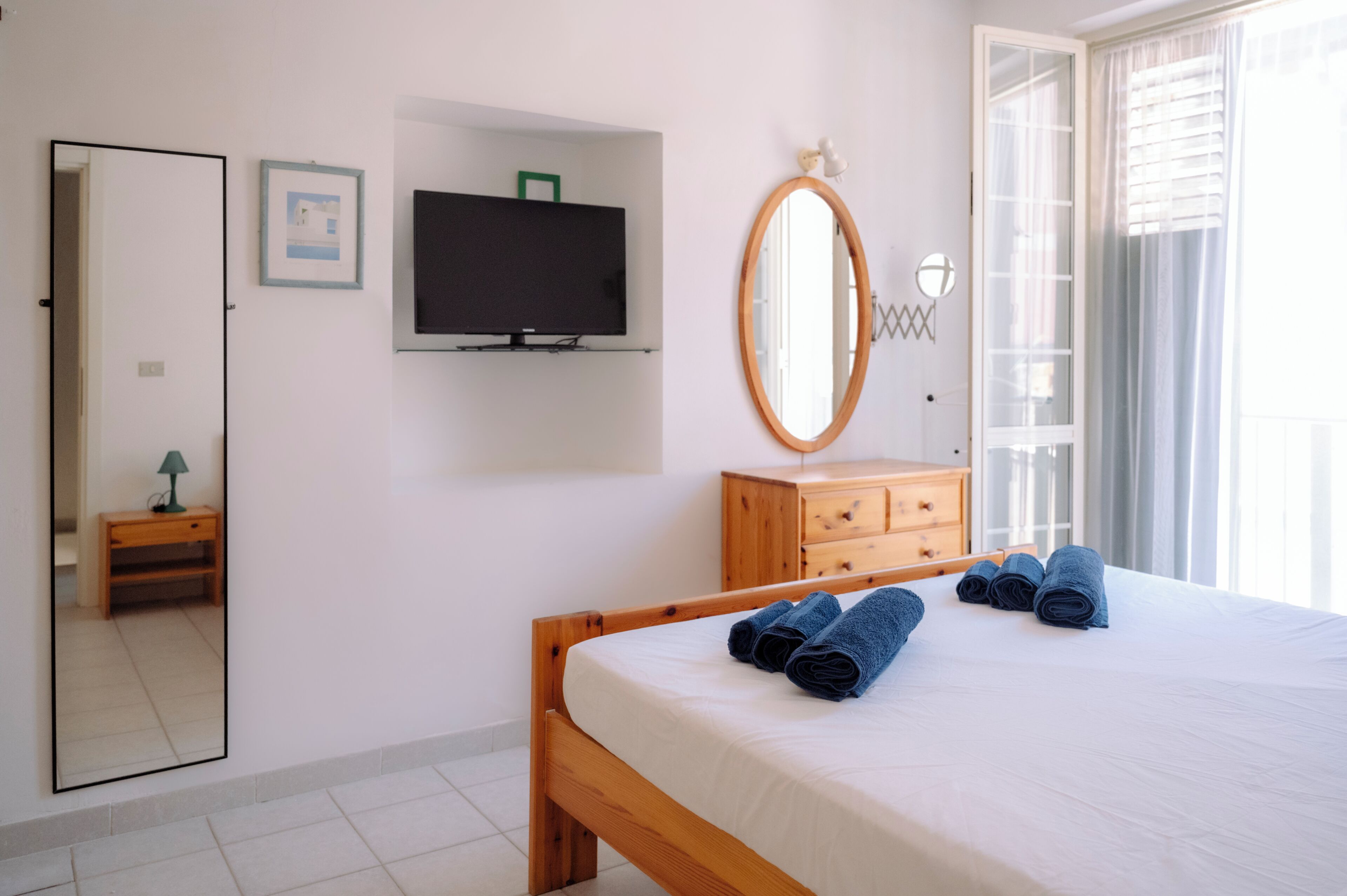 A bedroom with a bed, a dresser, a television, a mirror, and a door.