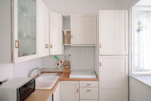 Una cocina compacta con gabinetes blancos, un lavamanos, una encimera y una ventana.