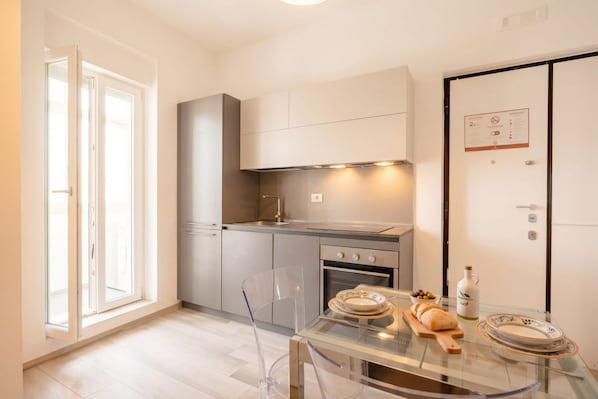 A modern kitchen with a glass table, stainless steel appliances, and a view of the outside. - Panorama Oberdan | Stylish Apartment in Bari (Bari)