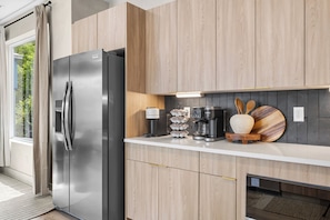 Eine moderne Küche mit einem Edelstahlkühlschrank, Holzschränken, einer Kaffeemaschine und einem Kaffeemühle auf der Arbeitsplatte.