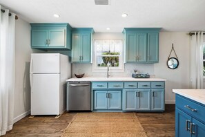 A kitchen with teal cabinets, a white refrigerator, and a wooden floor. - Private Hot Tub | Dogs Welcome | Grill (Port St. Joe)