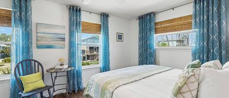A bedroom with a bed, a chair, a small table, and a window with curtains.