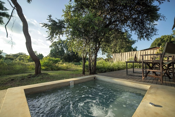 A hot tub surrounded by a wooden deck, with trees and a grassy area in the background. - Ceylon Wild (Yala)