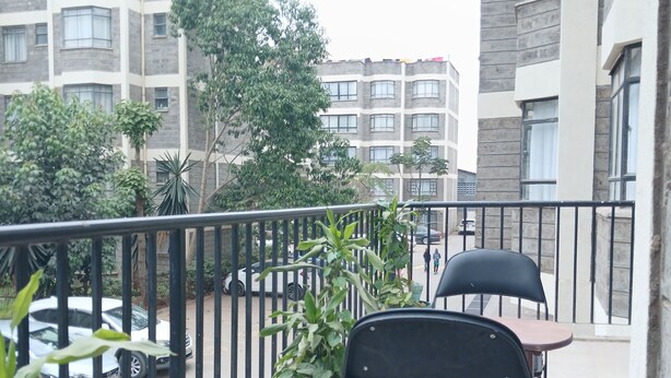 Un balcon avec une rambarde en métal, un pot de fleurs et une chaise noire.