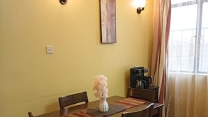 Un coin repas avec une table en bois, des chaises, un vase de fleurs, une machine à café et un tableau accroché au mur.