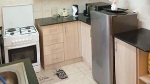 Une cuisine de taille réduite, équipée d’une cuisinière à gaz, d’un réfrigérateur et de meubles de rangement en bois.