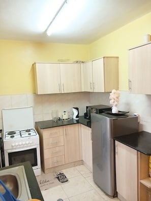 A compact kitchen with a gas stove, a refrigerator, and wooden cabinets. - The Terminal Residence (JWM9+X5X, Nairobi, Kenya)