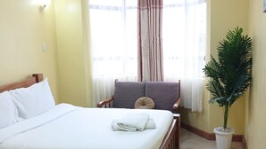 Une chambre à coucher avec un lit, une chaise, une plante en pot et une fenêtre avec des rideaux.