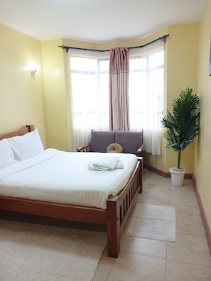 A bedroom with a bed, a chair, a potted plant, and a window with curtains. - The Terminal Residence (JWM9+X5X, Nairobi, Kenya)