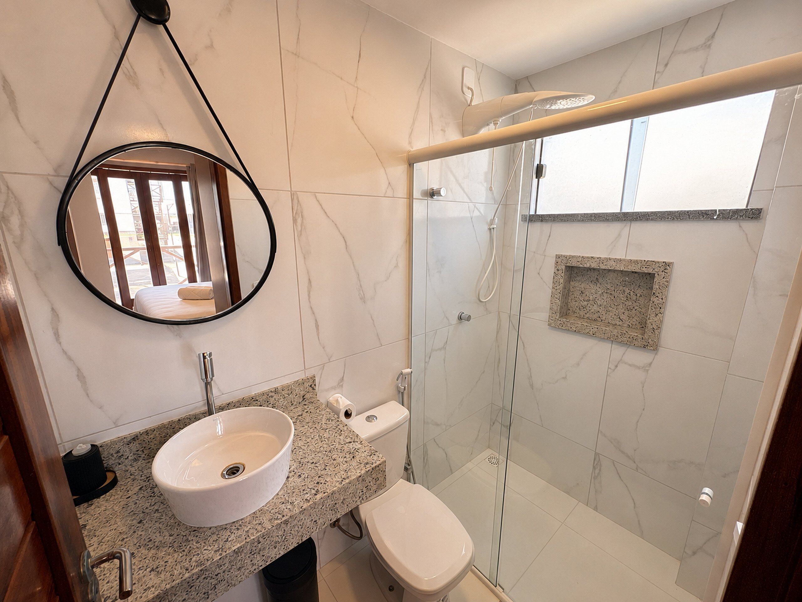 A bathroom with a round mirror, a sink, a toilet, and a glass-enclosed shower area.