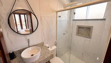 A bathroom with a round mirror, a sink, a toilet, and a glass-enclosed shower area.
