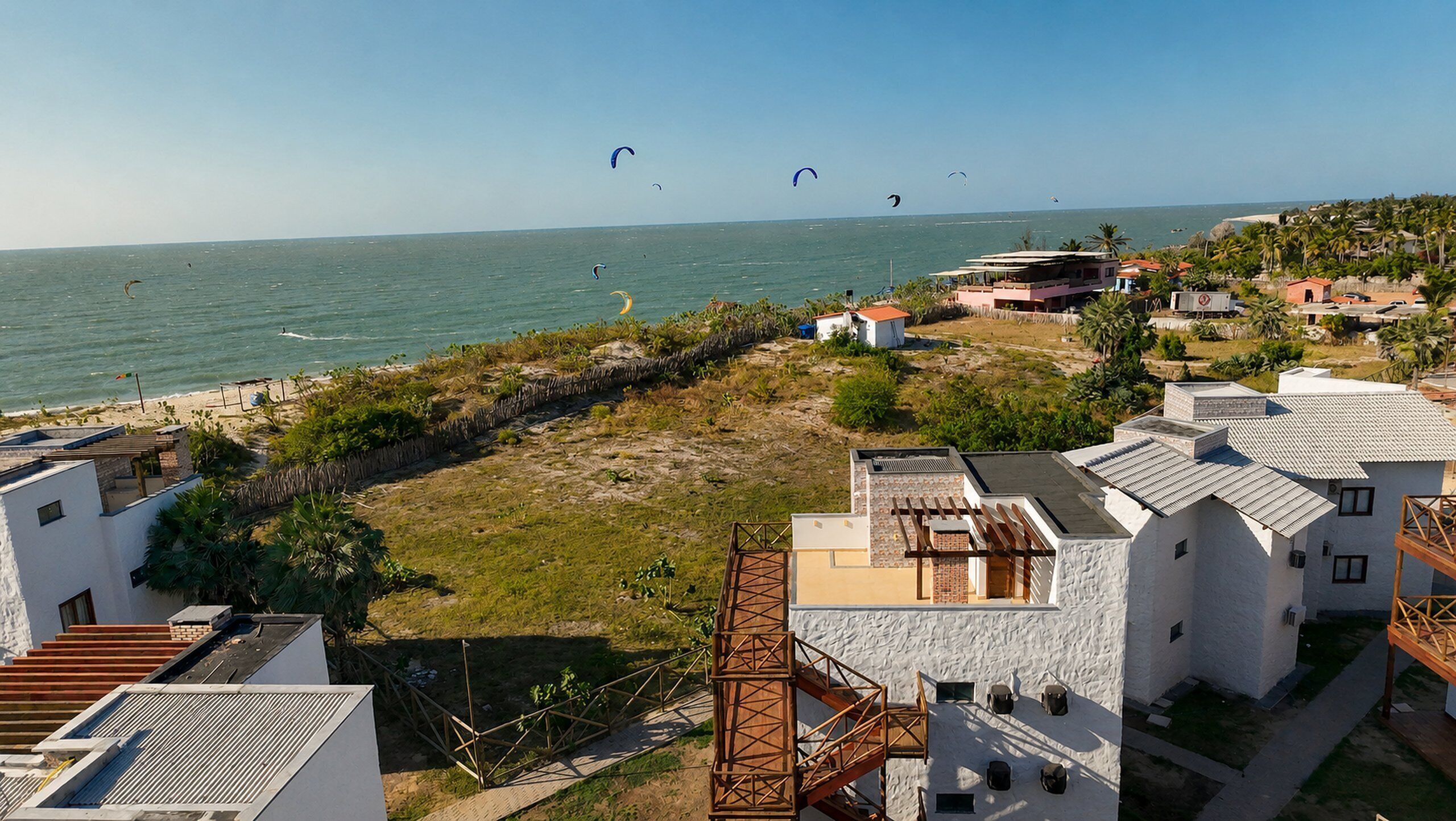 Een woongebied aan de kust met huizen, een strand en kitesurfers.