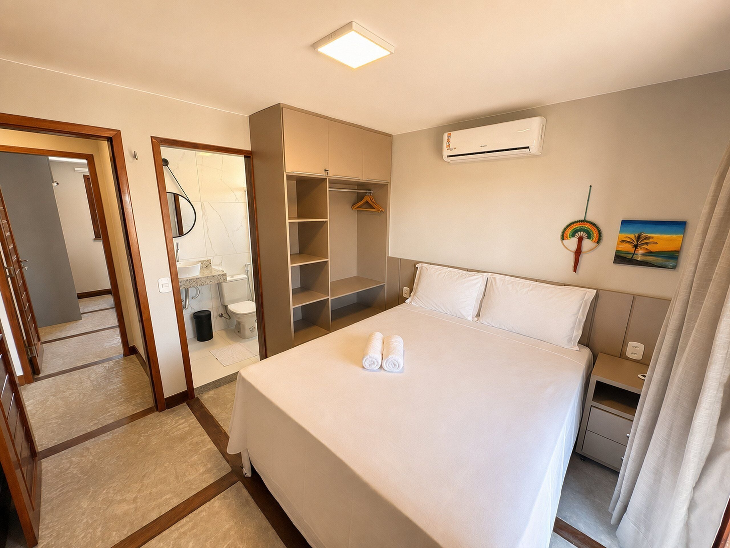 A hotel room with a bed, a wardrobe, a bathroom, and an air conditioning unit.