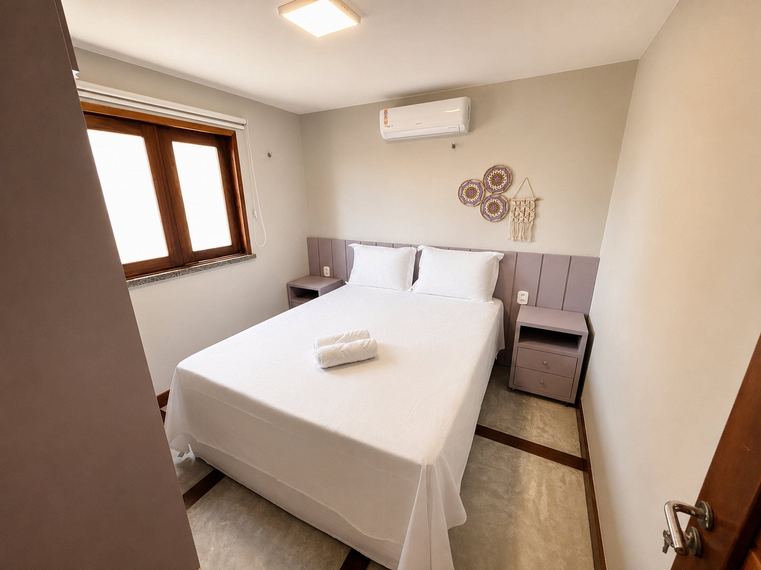 Une chambre à coucher avec un grand lit, une table de chevet, une commode, un appareil de climatisation et une fenêtre.