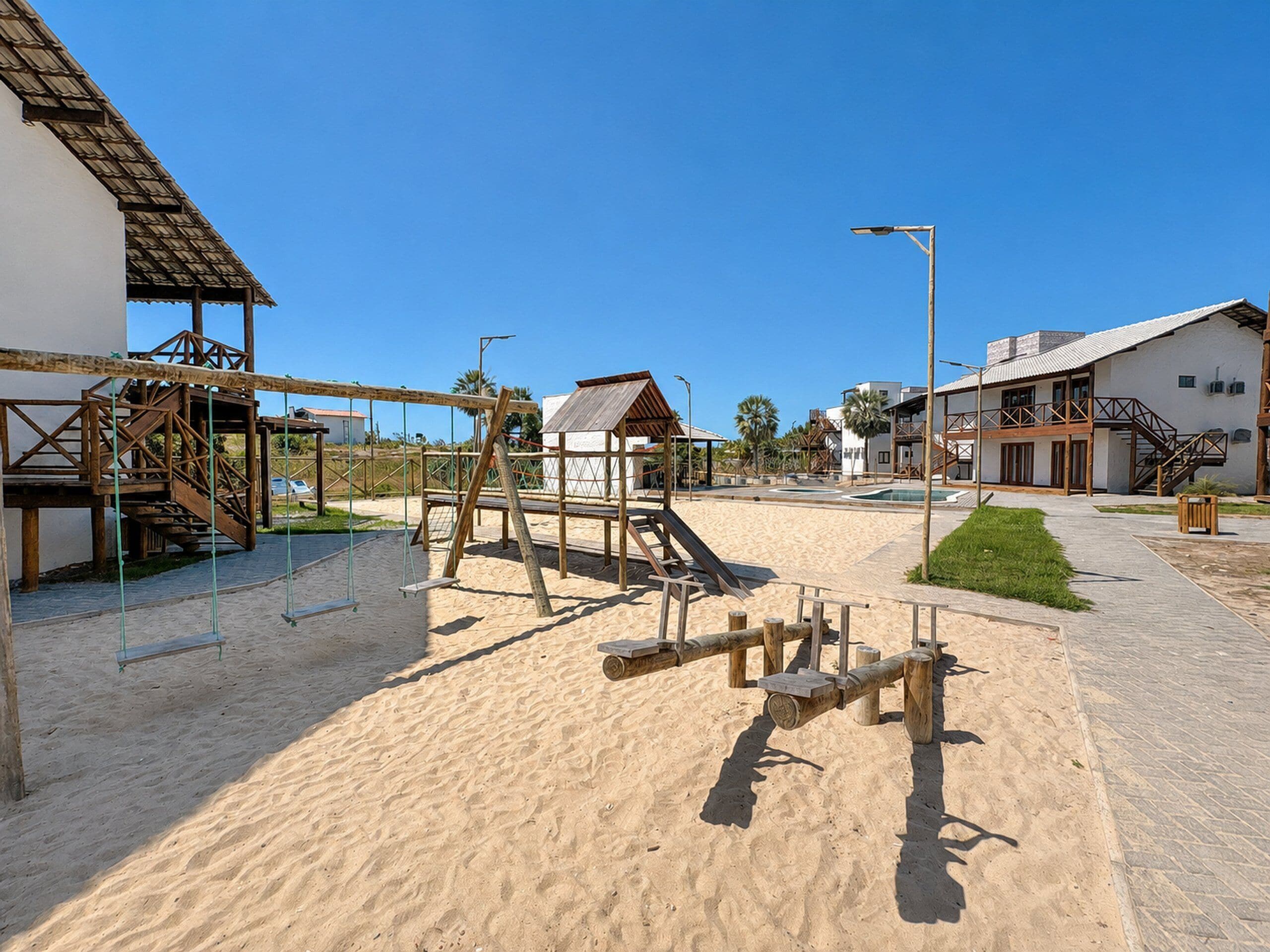 Un patio arenoso con estructuras de madera, una piscina y edificios con balcones.