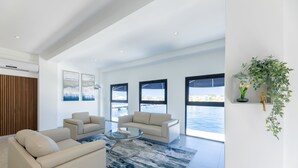 Een ruime woonkamer met een groot raam met uitzicht op een wateroppervlak, een moderne zithoek en een glazen salontafel.