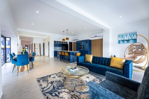A modern living room with a blue sofa, a coffee table, and a dining area with blue chairs. - Handelskade's Grand Historical Penthouse: Refined Luxury Living (Willemstad)
