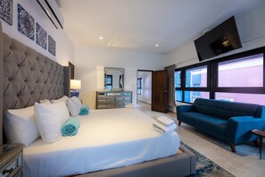 A hotel room with a large bed, a dresser, a mirror, a blue sofa, and a TV. - Handelskade's Grand Historical Penthouse: Refined Luxury Living (Willemstad)