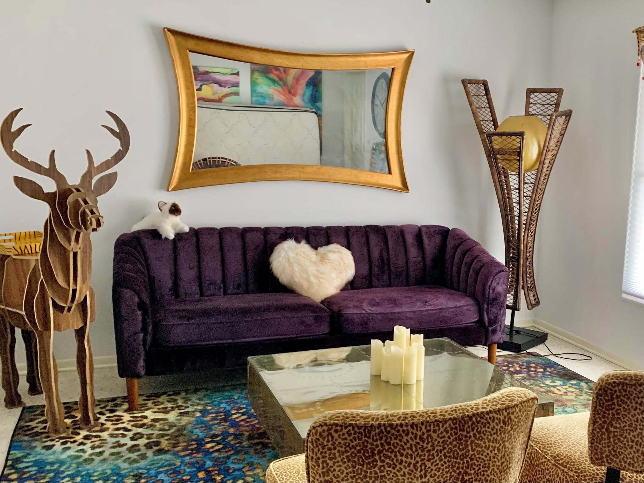 Un salón con un sofá morado, una mesa de centro de vidrio, un tapete de estampado de leopardo y una silla con estampado de jirafa.
