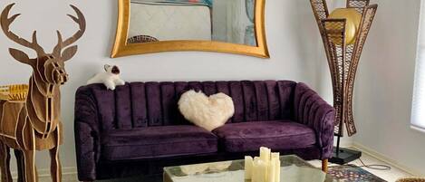 Un salón con un sofá morado, una mesa de centro de vidrio, un tapete de estampado de leopardo y una silla con estampado de jirafa.