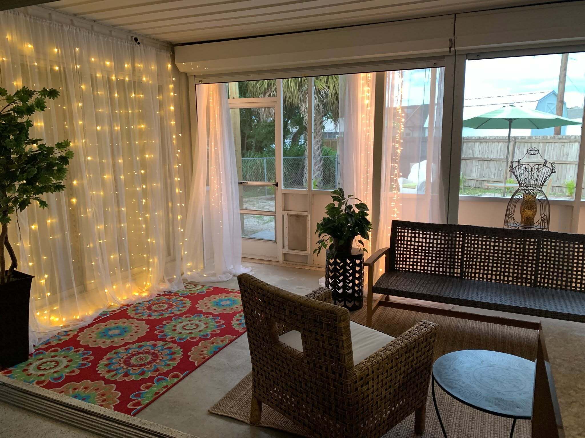A sunlit patio with a wicker chair, a small table, a decorative rug, and a potted plant.