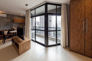 A modern living room with a large sliding glass door leading to a balcony, a wooden cabinet, and a seating area with a table and chairs. - Address by Bhomy (São Paulo)
