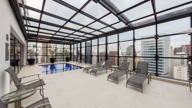 Terraço no telhado com piscina, espreguiçadeiras e vista para a cidade.