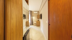 Um corredor de hotel com porta de madeira, espelho, televisão e mesa com cadeira.