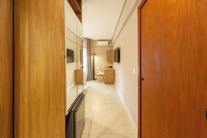 A hotel hallway with a wooden door, a mirror, a television, and a desk with a chair. - Address by Bhomy (São Paulo)