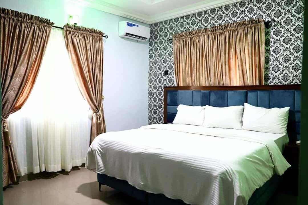 A bedroom with a bed, curtains, an air conditioning unit, and patterned wallpaper.