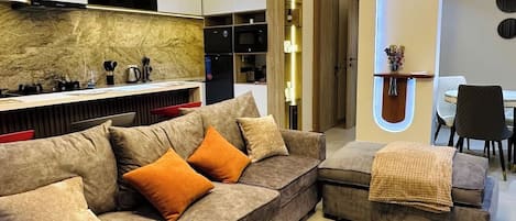 A modern living room with a sectional sofa, a coffee table, and built-in kitchen appliances.