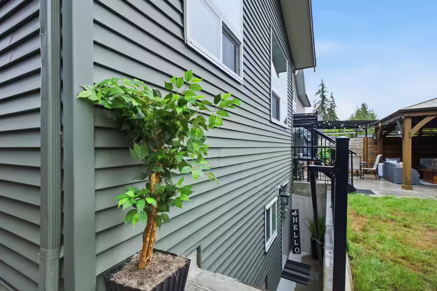 A residential building with a potted tree on the side, a covered outdoor seating area, and a visible staircase.