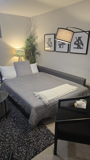 A bedroom with a bed, bedside tables, a lamp, framed artwork, and a potted plant.