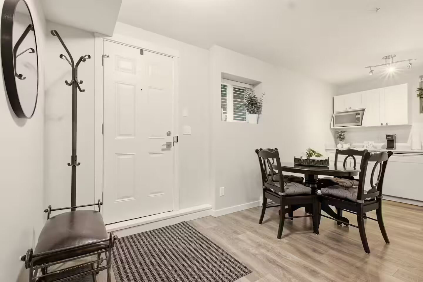A dining area with a table and chairs, a coat rack, a door, and a small window.