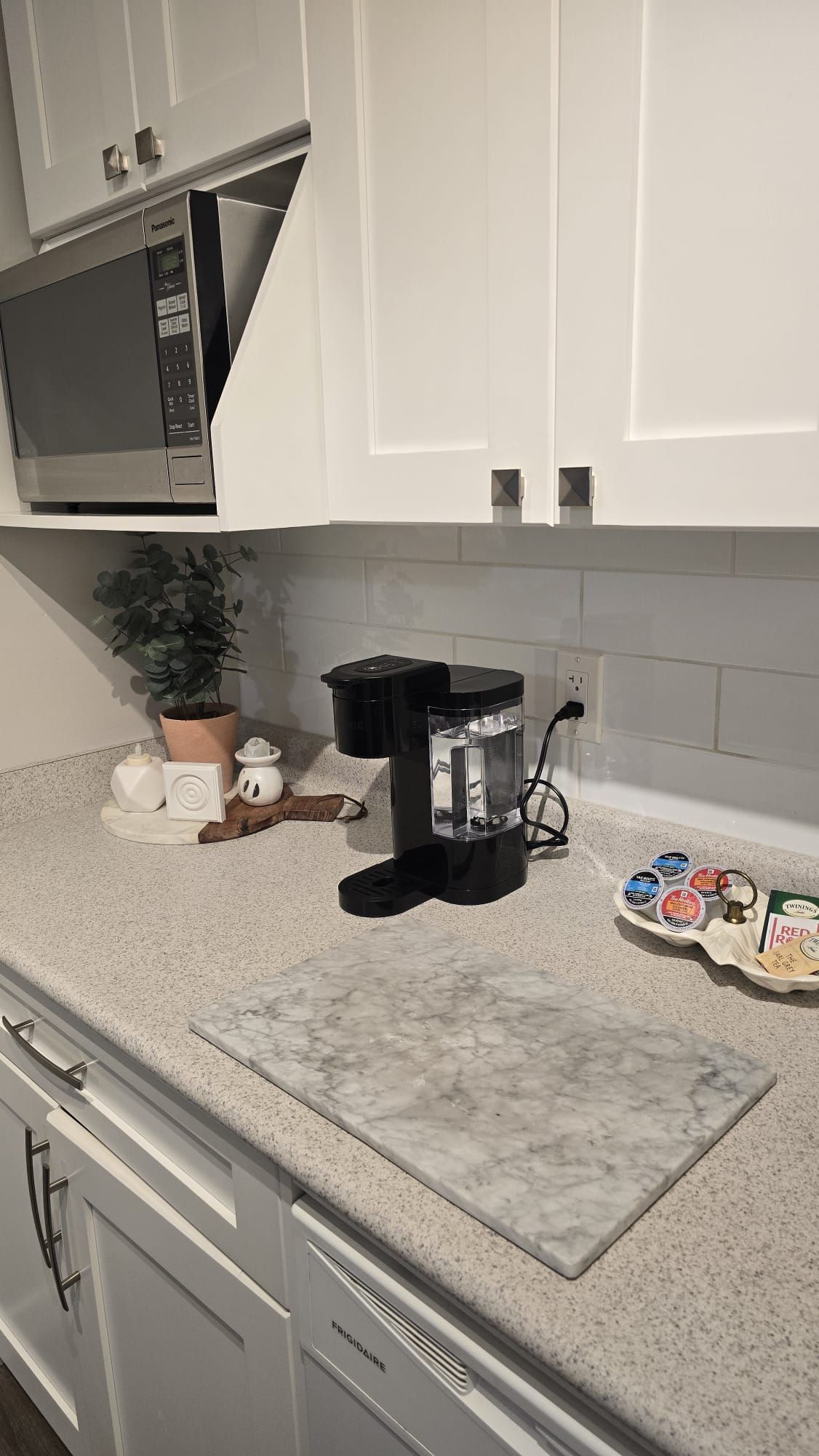 A kitchen with a microwave, coffee maker, and a marble countertop.