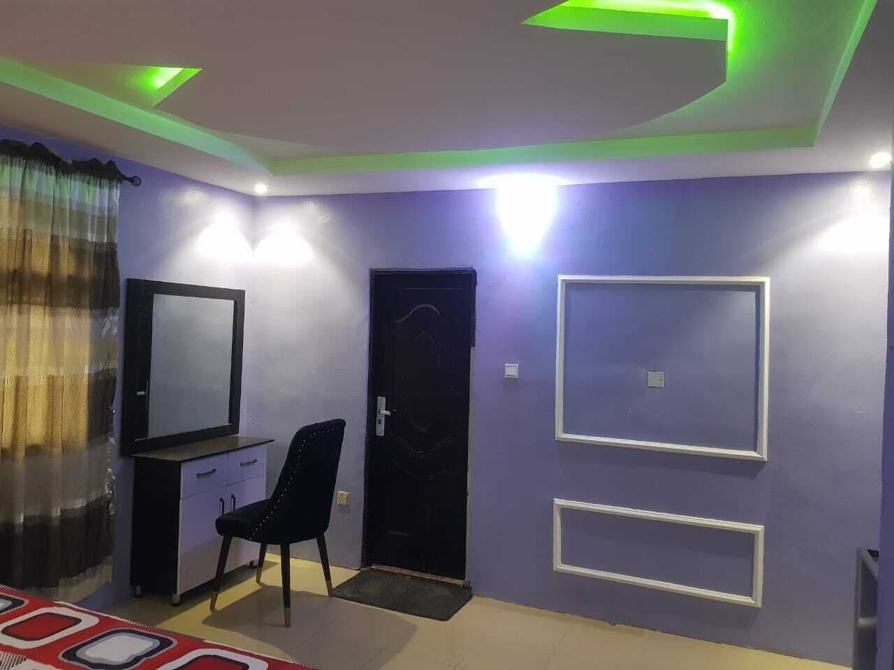 Una habitación con una puerta negra, un espejo, una silla y una pared con dos marcos rectangulares.