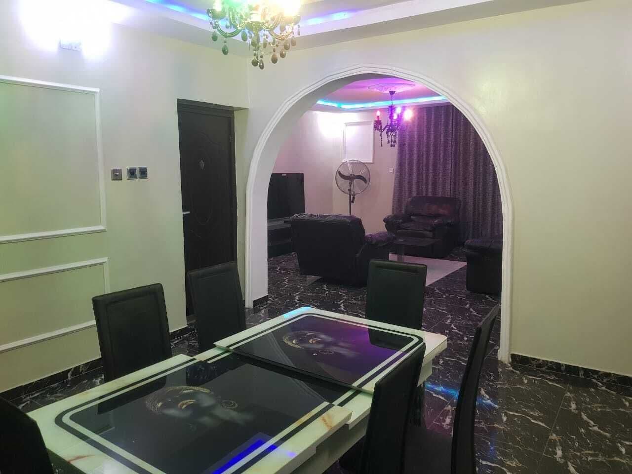 A conference room with a glass table, chairs, a chandelier, and a seating area with a curtain backdrop.