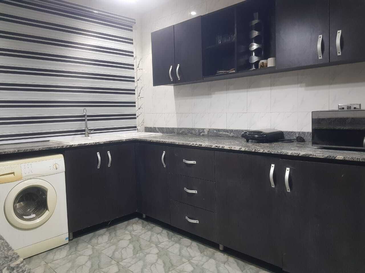 Una cocina con armarios oscuros, lavadora y microondas.