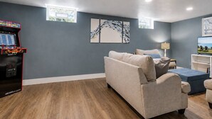 Ein Wohnzimmer mit grauem Sofa, blauem Hocker und einem Retro-Spielautomaten.