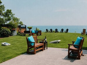 An outdoor seating area with wooden chairs and tables, a bottle of wine, and a view of the ocean.