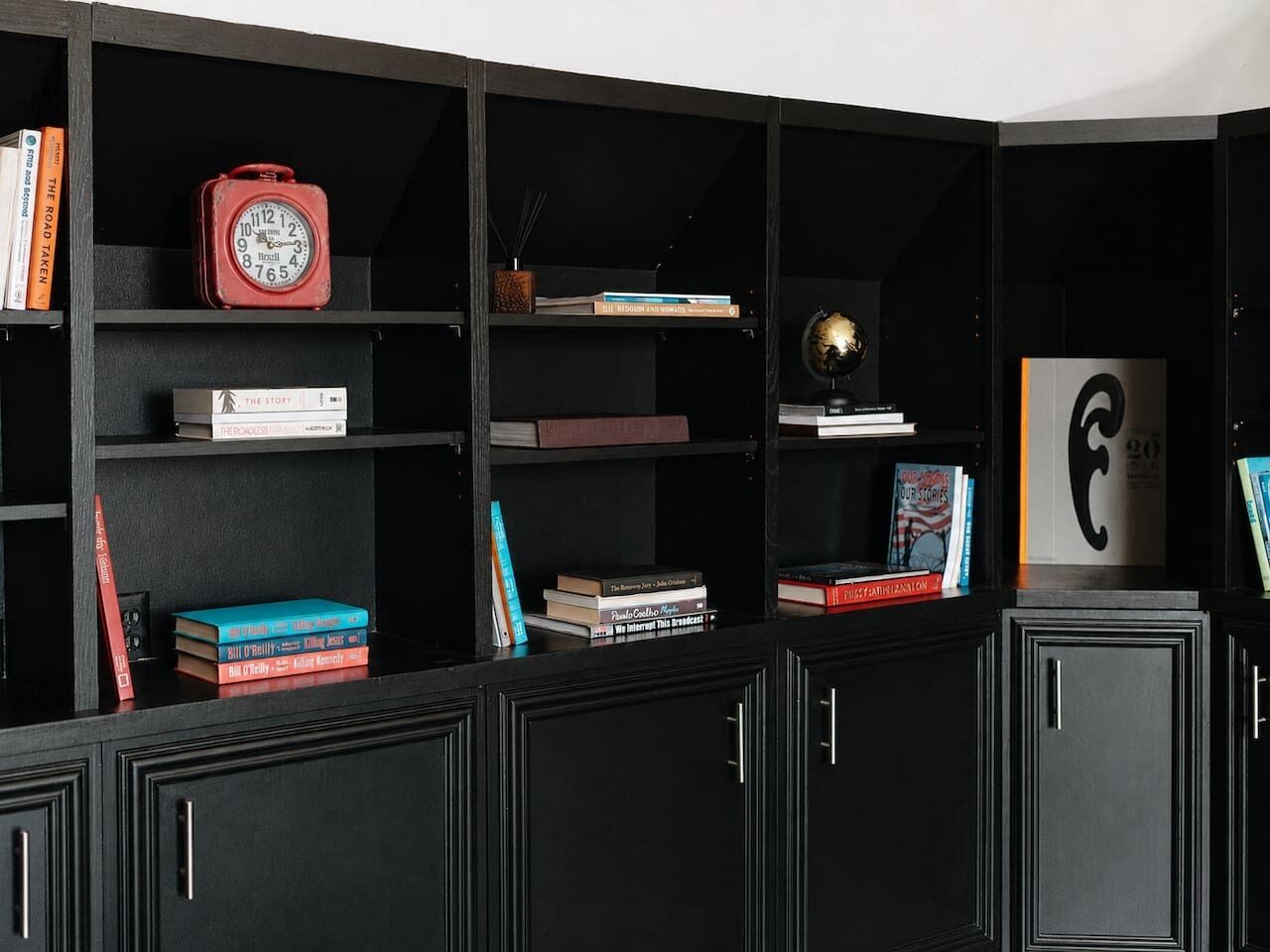 Une bibliothèque noire contenant divers ouvrages, une horloge rouge et un globe terrestre.